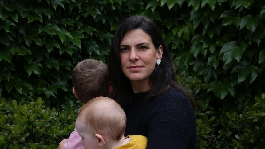 A woman looking serious holds her two children