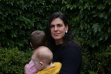 A woman looking serious holds her two children