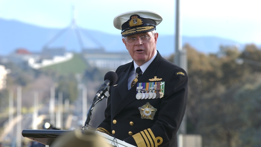 Chris Barrie in full navy uniform delivering a speech with Parliament House in the background