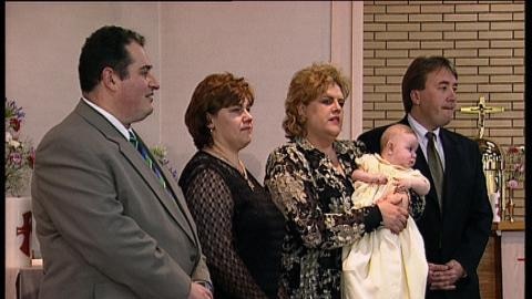 A group of four adults and one baby stand in a church at a baptism