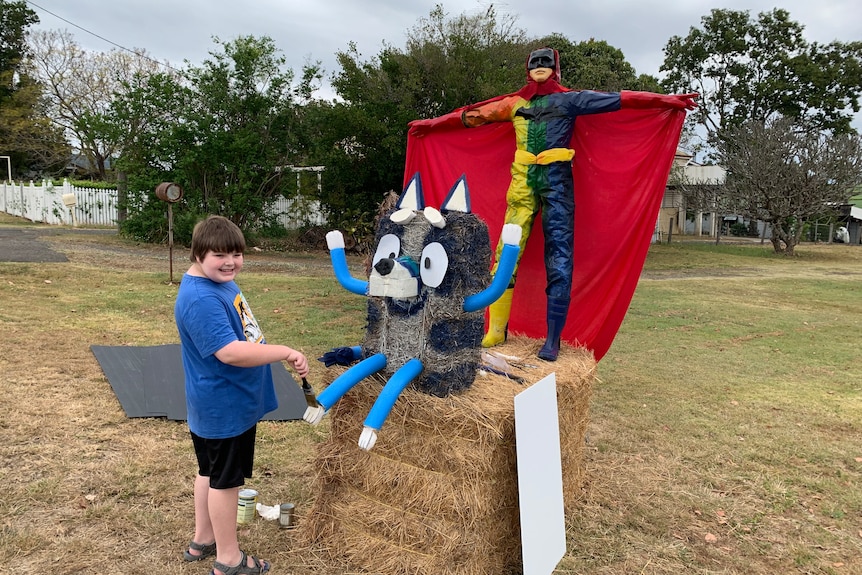 Young boy stands paints his haybale art of Bluey and Batman