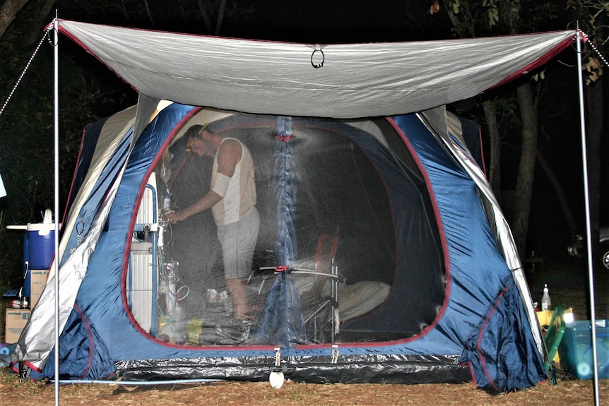 A man in a tent at night, concentrating on something through the gauze.