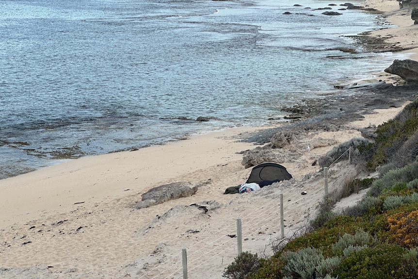 tent on the sand with towel and belongings outside. Ocean in the background.