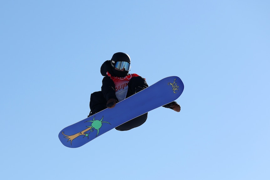 A snowboarder tucks her legs and board in while mid-air during a competition at the Winter Olympics.
