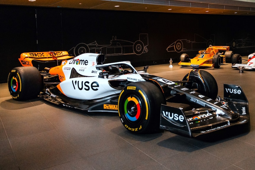 An F1 car in a show room, black at the front, white in the middle and orange at the back, on display.