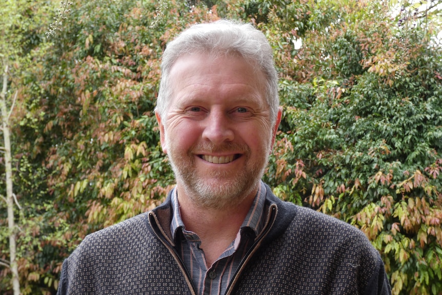 A man smiling in front of some trees