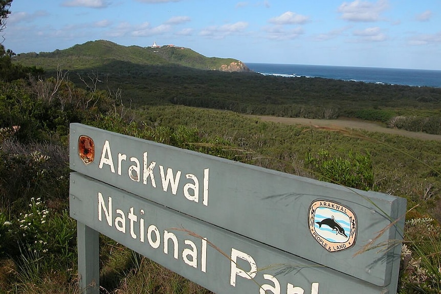 A wooden sign reading 'Arakwal National Park', with the ocean visible in the background.