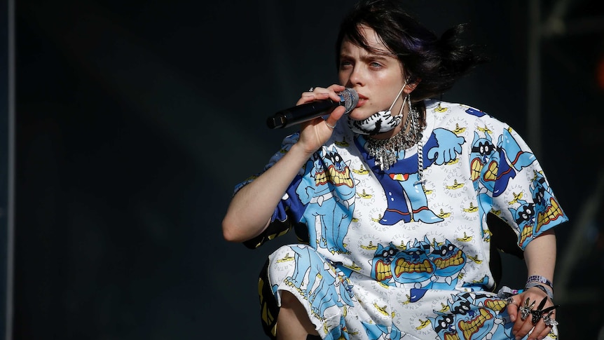 Billie Eilish crouches down on stage to sing at Glastonbury Festival.