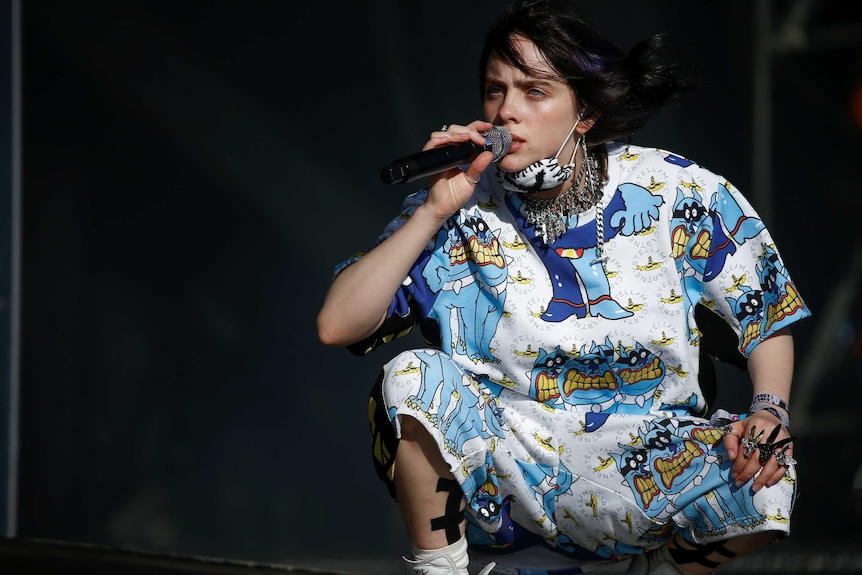 Billie Eilish crouches down on stage to sing at Glastonbury Festival.