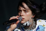 Billie Eilish crouches down on stage to sing at Glastonbury Festival.