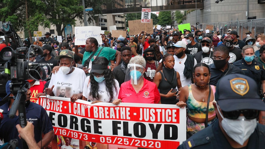 A crowd of black people, some wearing face masks, hold up colourful banners on a city street.