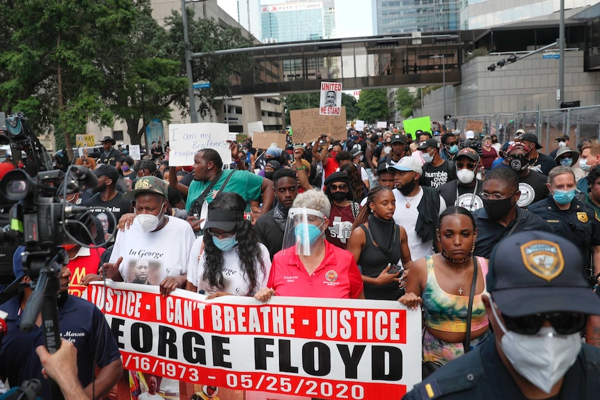 A crowd of black people, some wearing face masks, hold up colourful banners on a city street.