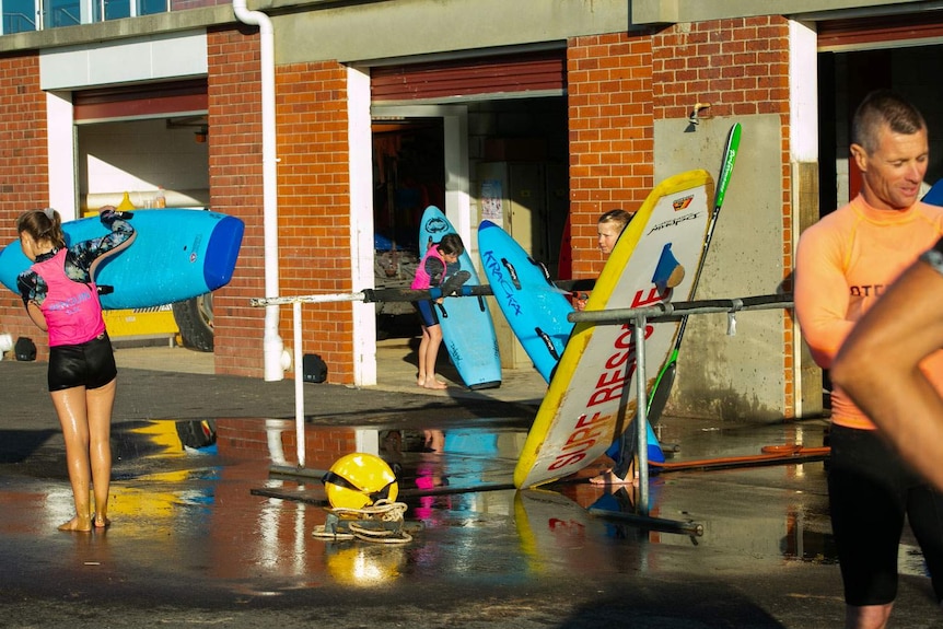 Young and old surf club members wash down paddle boards outside the club house