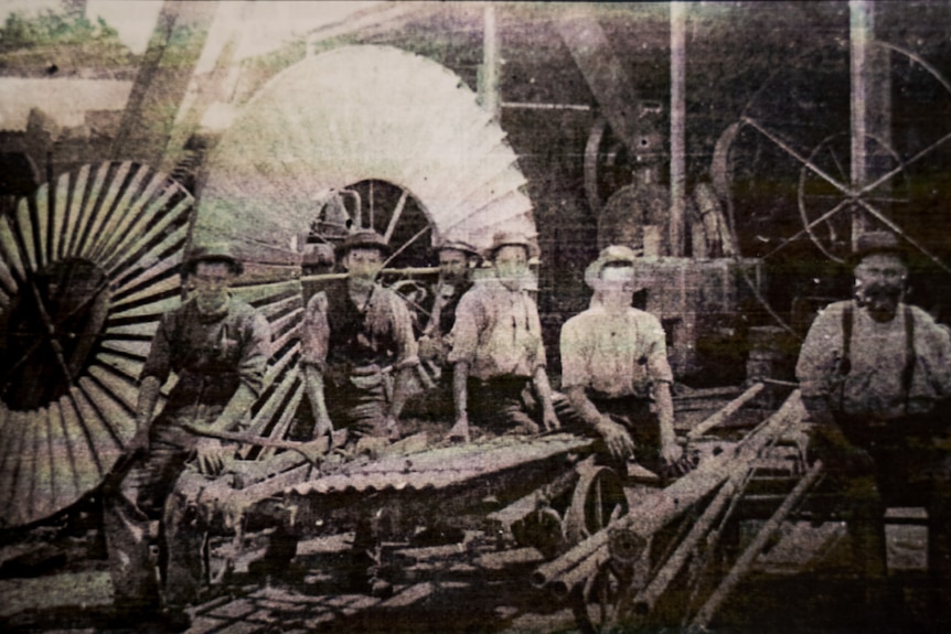 A black and white photo from 1900 of a group of men in front of windmill wheels.