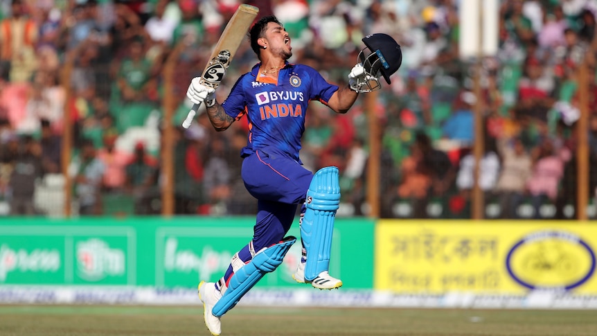 An Indian male batter jumps in the air with his bat as he celebrates an ODI double century.