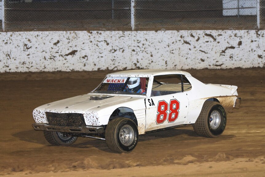 a white car with a red 88 on the door and wacka on the windshield with mud splattered on it from the race track