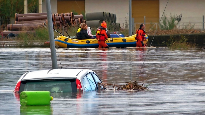 Rescue workers pulling a boat along, wade on a flooded street at San Gavino Monreale in Sardina on November 18.