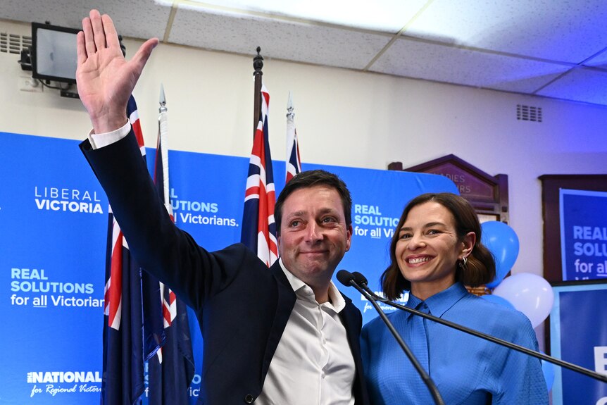 Matthew Guy waves his hand in the air with his wife by his side.