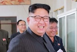 Kim Jong Un smiles and is surrounded by smiling military types as they look at a diagram.