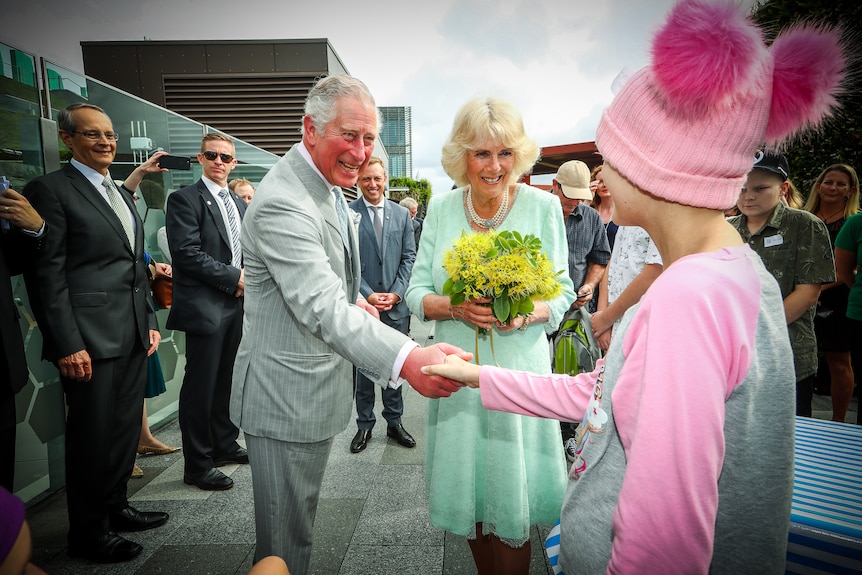 Le prince Charles et Camilla saluent une fille portant un bonnet rose avec deux pompons devant un hôpital de Brisbane.