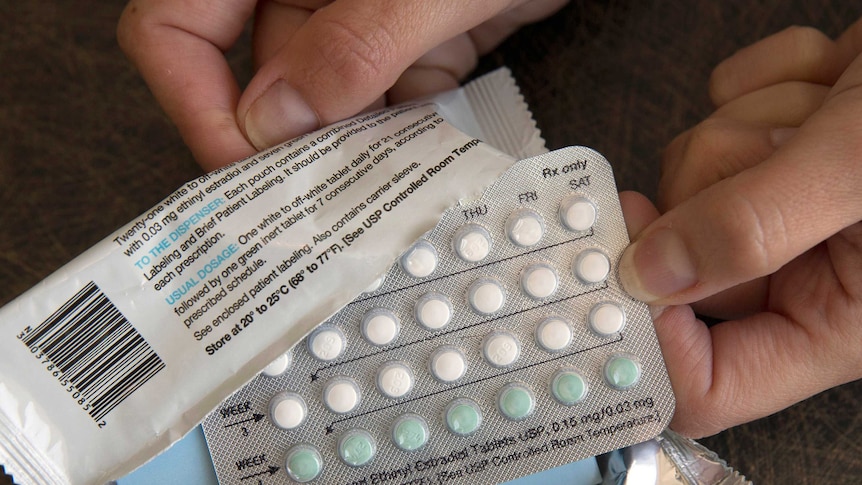 Disembodied hands hold open a pack of hormonal birth control pills.