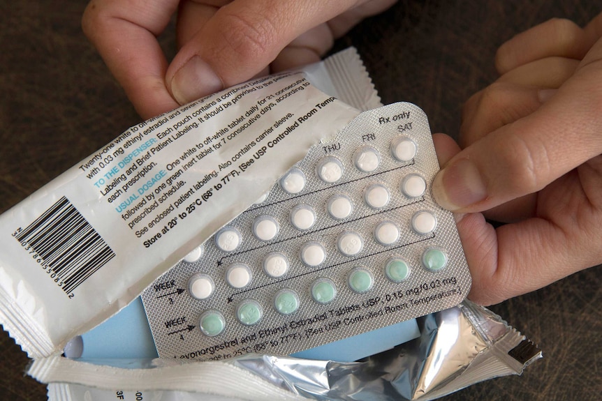 Disembodied hands hold open a pack of hormonal birth control pills.