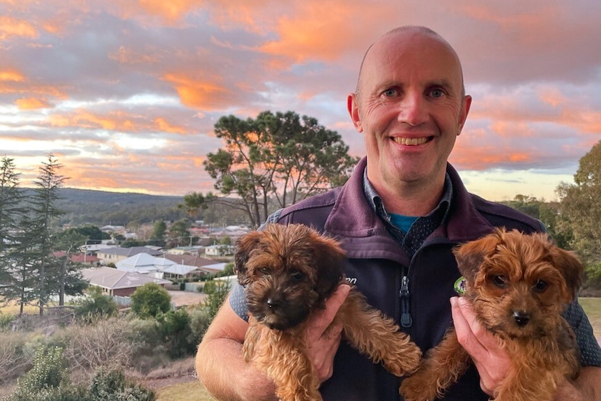 a man holds two dogs in fornt of a lovely sunset