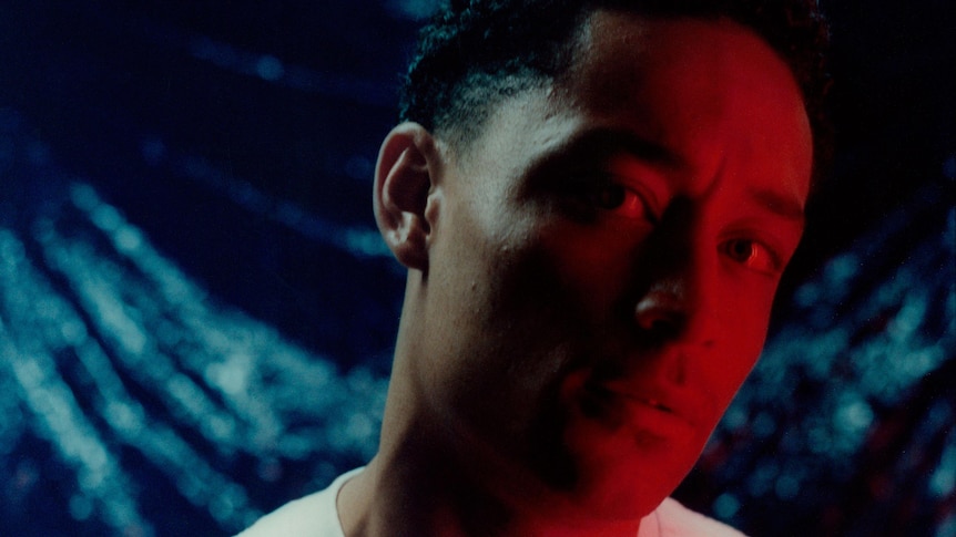 Close-up photo of Loyle Carner wearing a white t-shirt, staring at the camera