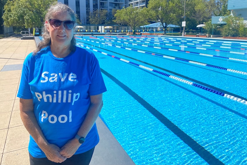 A woman stands in front of an outdoor lane pool with a short that reads "Save Phillip Pool".
