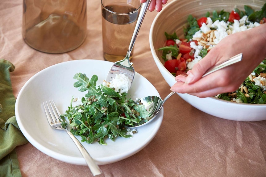 Lentil, rocket and pesto salad with feta cheese and cherry tomatoes being served in a bowl on a table setting.