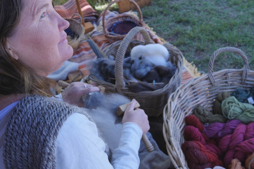A woman is sitting on a blanket surrounded by baskets of wool. She's looking up.
