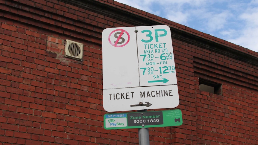 Parking restriction messages are displayed on a white sign in front of a red brick wall.