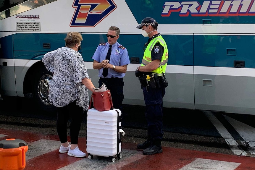 A woman speaking to a bus driver and a policeman wearing a protective mask