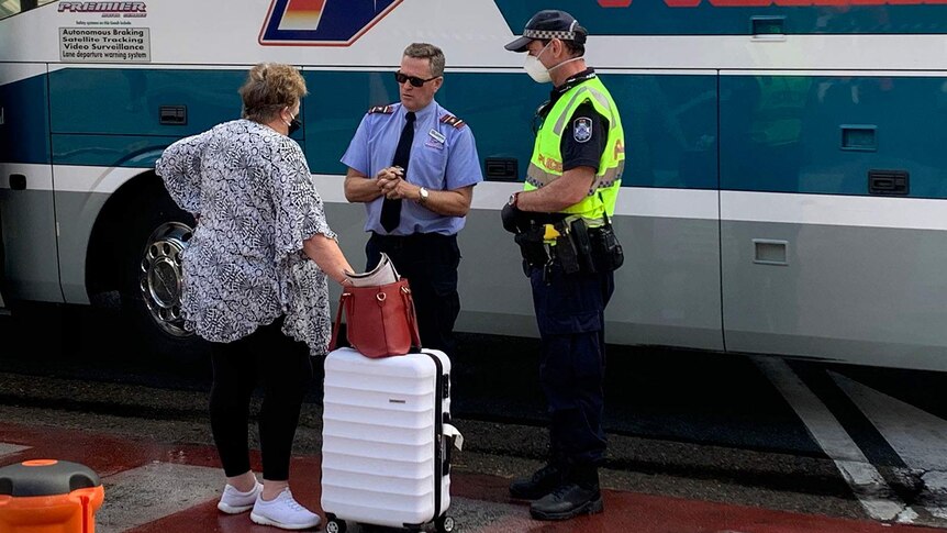 A woman speaking to a bus driver and a policeman wearing a protective mask