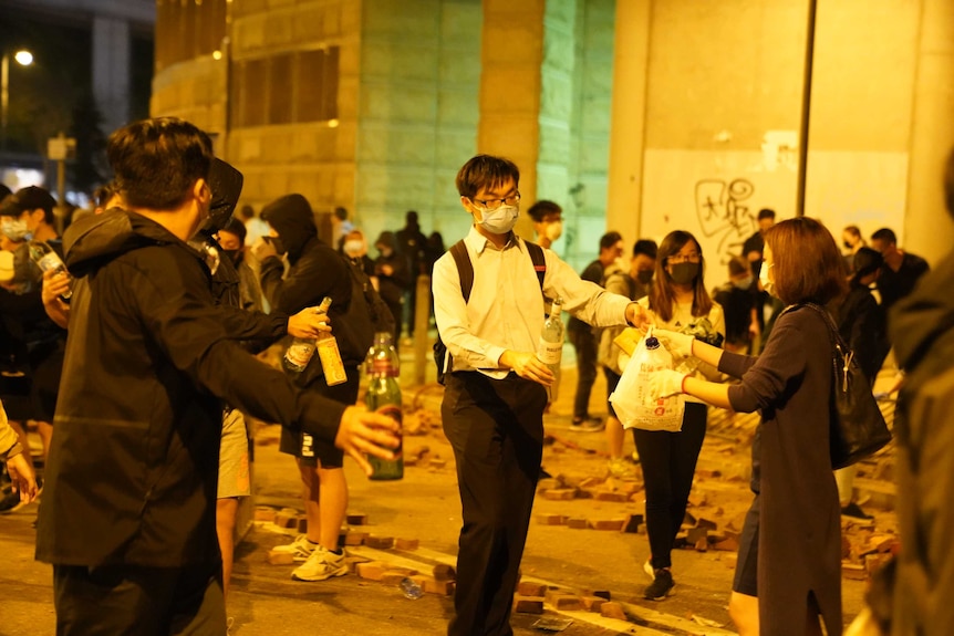 A crowd of protesters are on a brick-strewn street exchanging the materials to make a molotov cocktail.