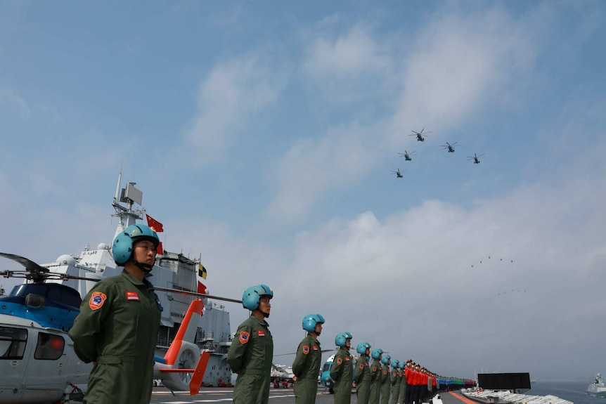 Navy personnel of Chinese People's Liberation Army stand in line, there are military aircrafts above and behind them.