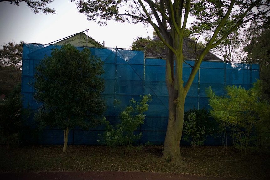 A house covered in scaffolding and blue tarps at dusk