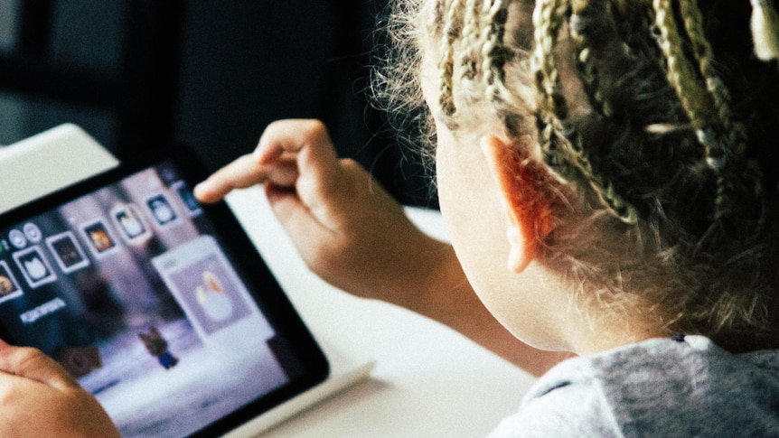 A kid with braids raises their finger to use a tablet screen