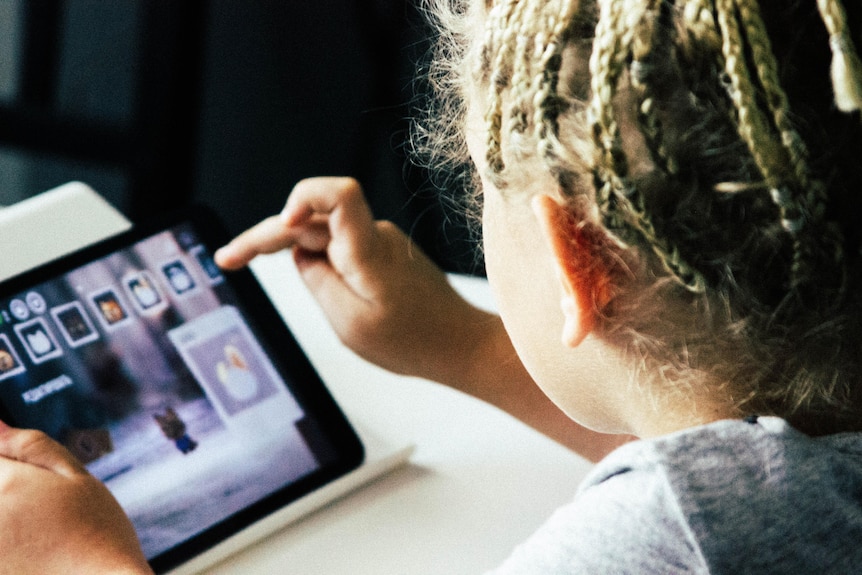 A kid with braids raises their finger to use a tablet screen