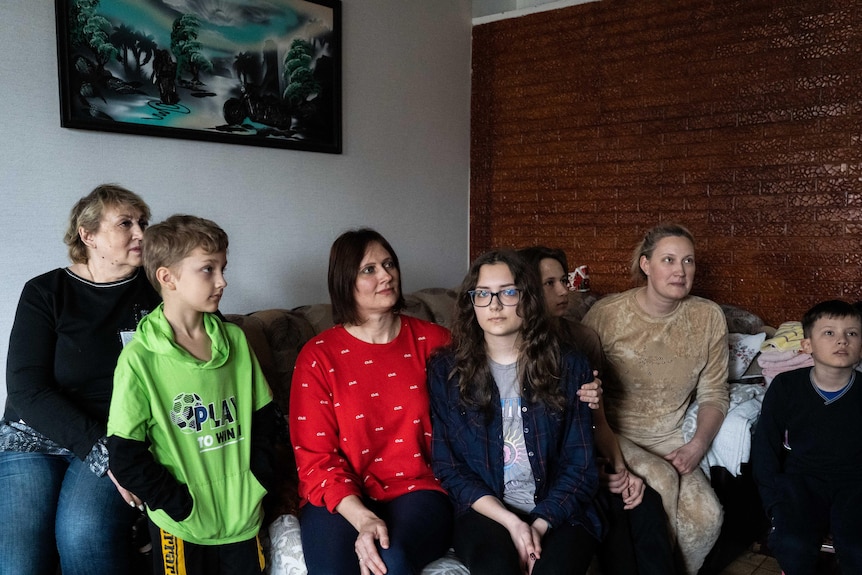 A family including a grandmother, two mothers and their children, sit together on a couch