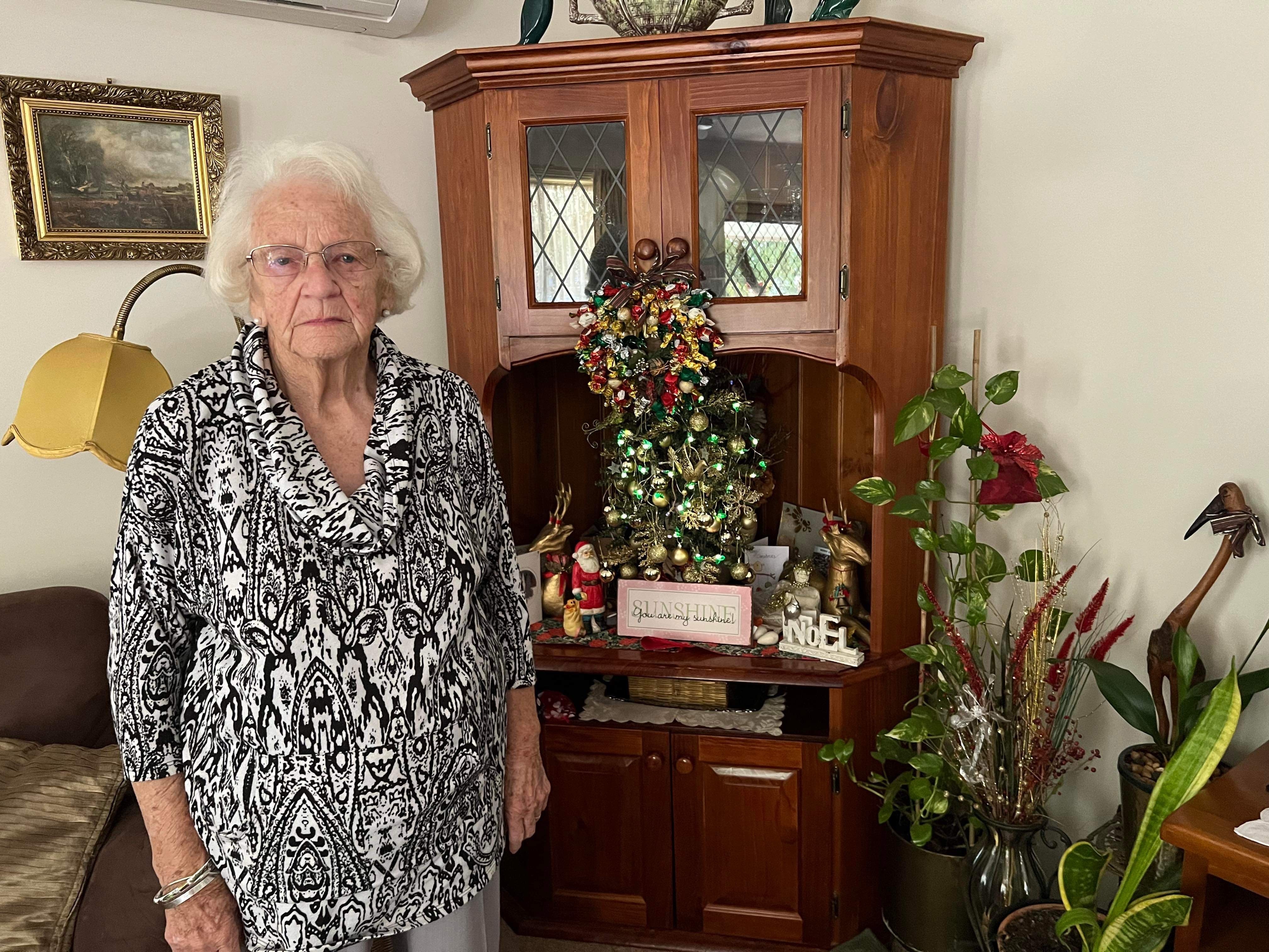 An elderly woman in a black and white dress in front of a Christmas tree.