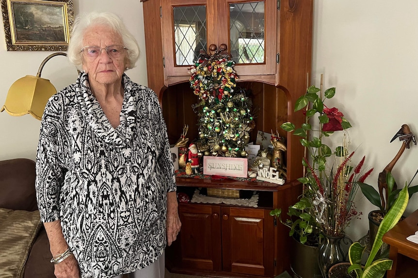 An elderly woman in a black and white dress in front of a Christmas tree.
