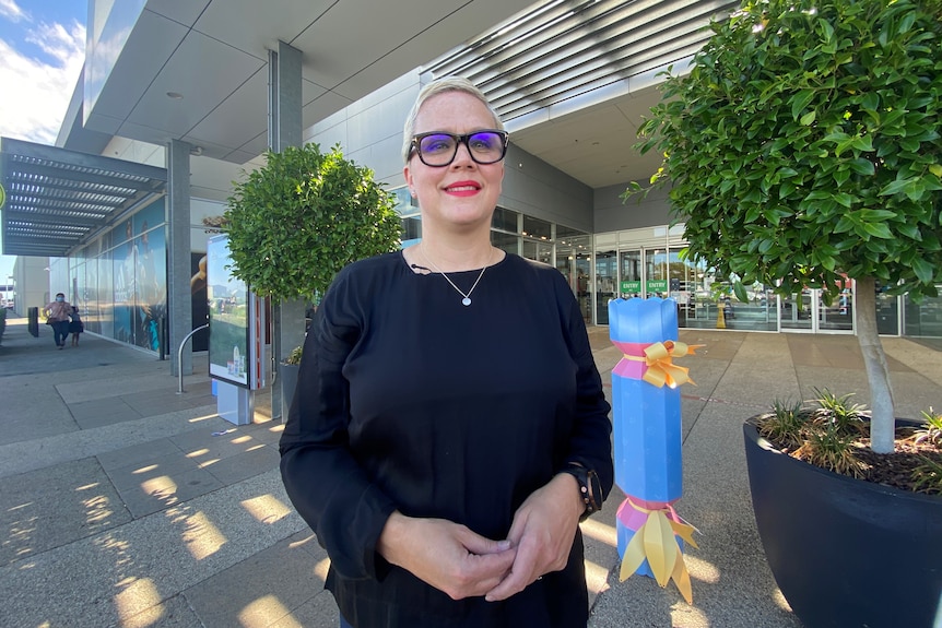 a woman with glasses infront of a shopping centre