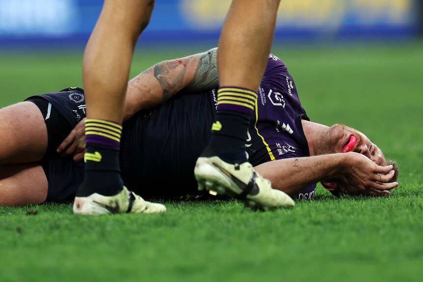 Cameron Munster lies on the ground holding his face and groin after getting injured during a Melbourne Storm NRL game.