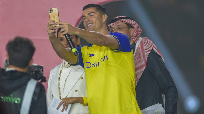 A man in a yellow soccer jersey takes a selfie with a phone.