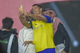 A man in a yellow soccer jersey takes a selfie with a phone.