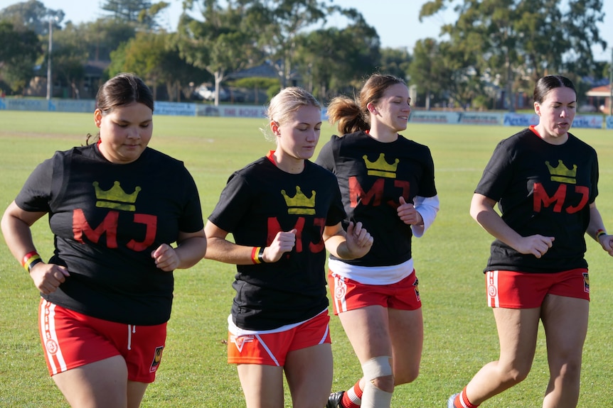 Four women running together on a football field