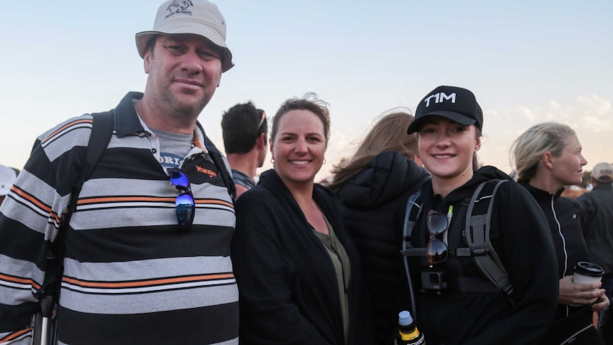 Noel and Kelly Derks and their daughter, all in walking gear, look at the camera with the morning light behind them.