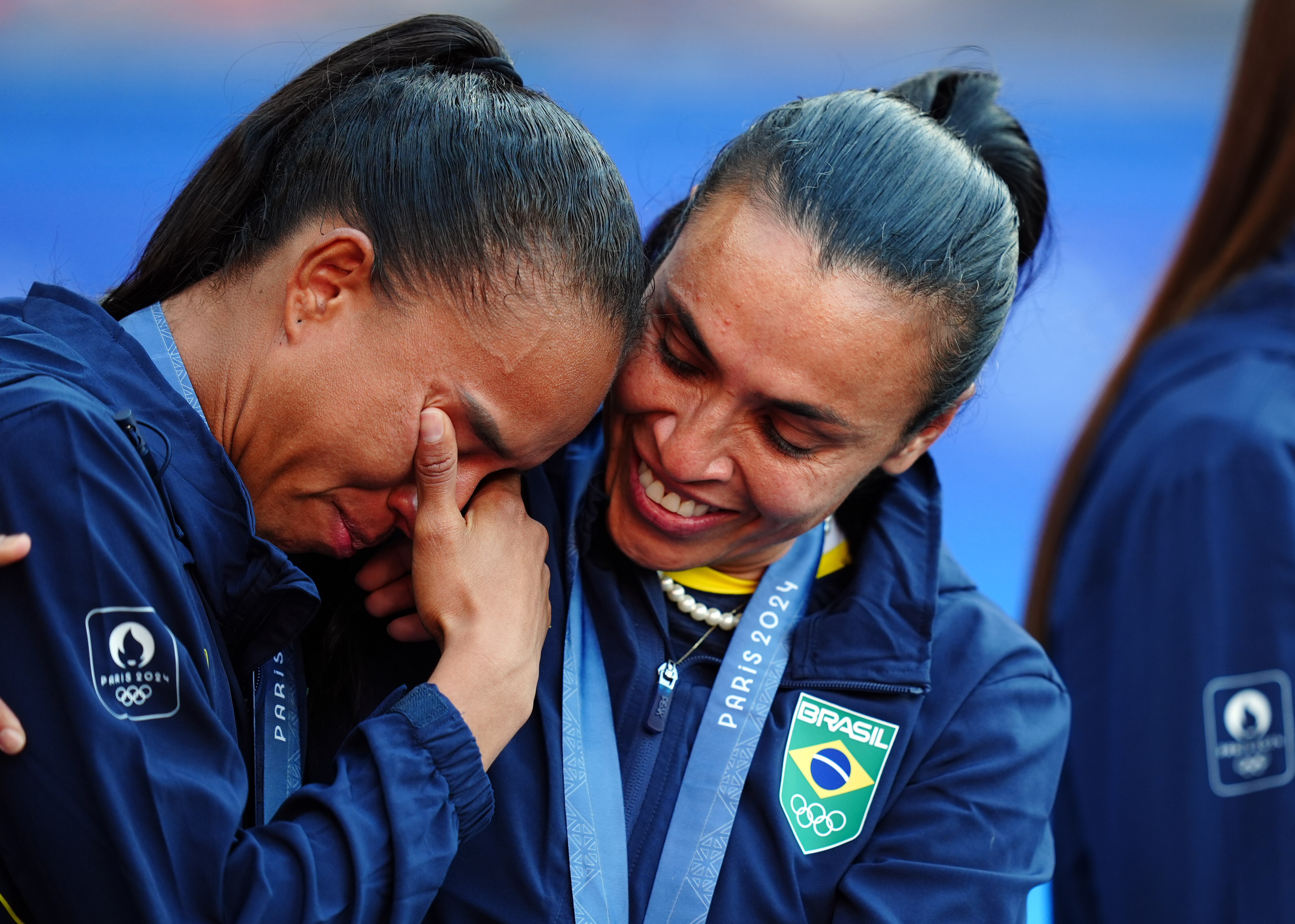 A woman in a blue jacket with a Brazil logocomforts a teammate who is crying