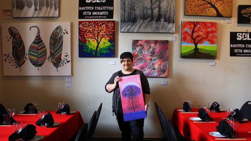 Mackay artist Nekea Blagoev stands inside a Mackay restaurant surrounded by her colourful paintings of trees